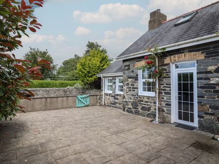 A stone house with a paved patio and a small blue gate in the garden at Bwthyn y Gwas in Tywyn