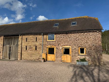 A stone barn with wooden doors and windows under a blue sky at Barn Cottage in Ludlow