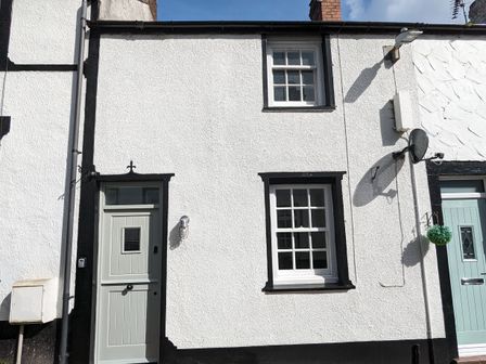 A white exterior house wall with two windows and a light green door in Conwy