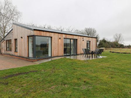 A wooden house with large windows and a patio with outdoor chairs and table on grass at The Cook House in Erlestoke near Great Cheverell