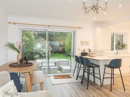 A kitchen and dining area with a wooden table and chairs next to sliding glass doors at 15 Maes Awel in Abersoch