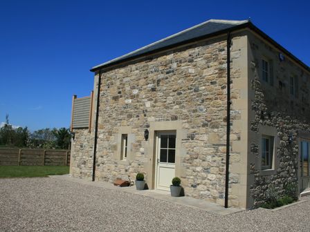 A stone house with a gravel driveway and two potted plants at Breakers in Bamburgh
