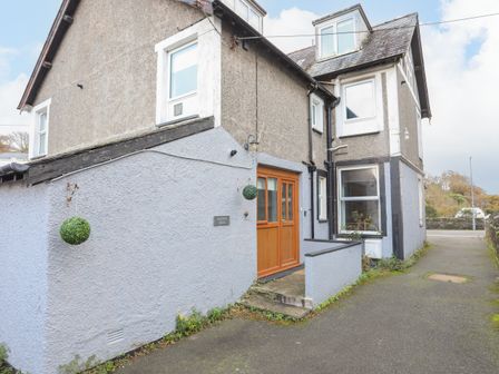 An exterior view of a two-story house with grey and light blue walls wooden double doors and hanging green ball decorations at Gweldon - Anchor Deck in Borth-y-Gest near Porthmadog