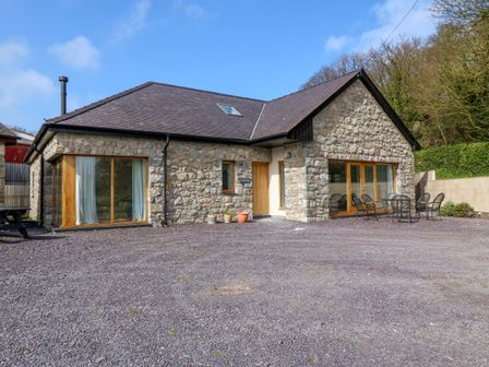 A stone house with large windows and a seating area outside at Yr Hen Dairy Penmon near Beaumaris