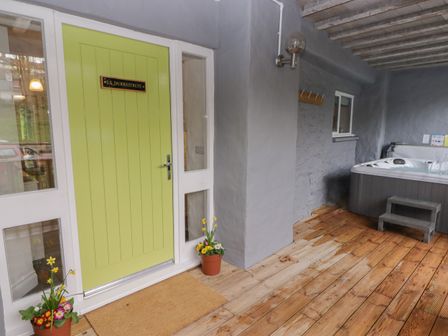 A covered outdoor area with a green door, two flower pots, wooden floor, and a hot tub at Le Durkestrete Cellar in Haverfordwest