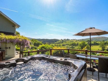 An outdoor patio with a hot tub table umbrella and chairs overlooking green fields at Curtau Llanfaredd near Builth Wells