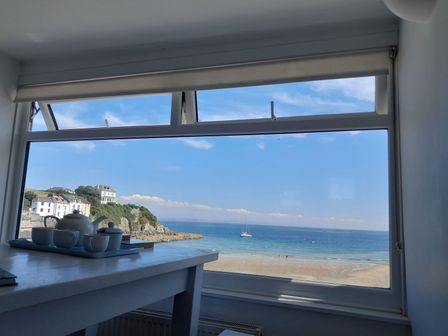 A table with a teapot and cups by a large window showing a beach sea and houses at The Loft at Beach House in Portmellon near Mevagissey