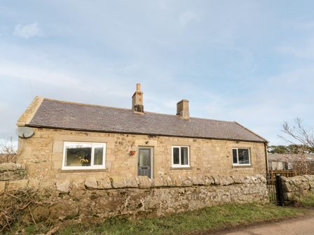 A stone cottage with three windows a door and two chimneys behind a stone wall at Moorlaws Farm in Alnwick