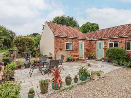 A courtyard with potted plants a table with chairs and a brick building with green doors at Millers Cottage Old Malton near Malton