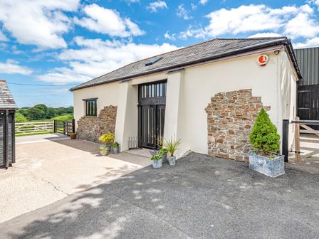 An exterior view of a converted barn with stone and plaster walls and potted plants outside at Waterland Old Barn in Bradworthy