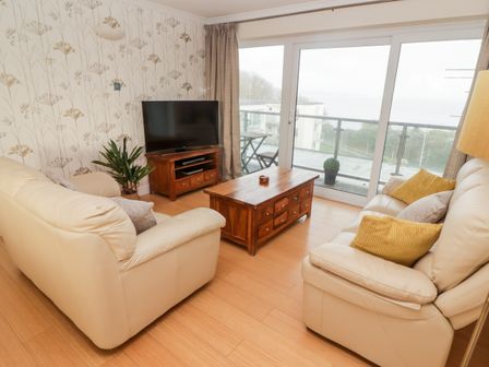 A living room with two beige sofas a wooden coffee table a flat screen tv and sliding glass doors leading to a balcony at 54 Croft Court in Tenby
