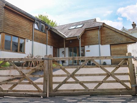 A wooden gate in front of a house with wooden and white walls and sloped roof at Little Rondeval in Totnes