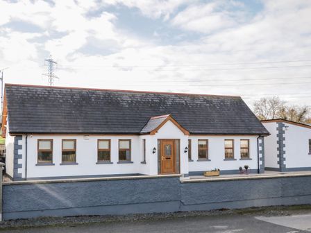 A single-story house with a dark roof and white walls with multiple windows and a central wooden door at The Garden Cottage in Crossmaglen