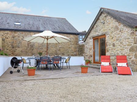 An outdoor patio with a dining table under an umbrella chairs barbecue and two red lounge chairs at Riviere Barton in Hayle
