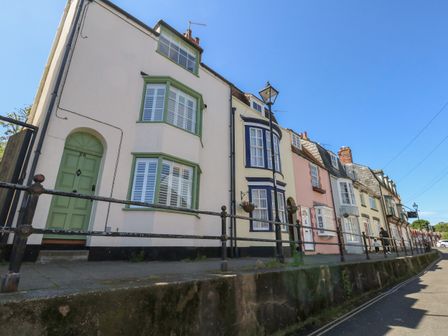 A row of terraced houses with colorful doors and windows along a street with railings and street lamps at Belvedere Cottage in Weymouth