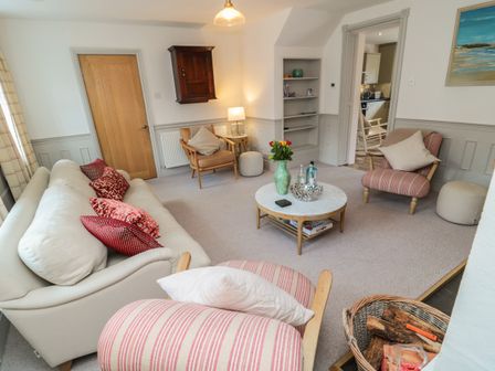 A living room with sofas armchairs a coffee table and a basket of firewood at Eider Cottage in Warkworth