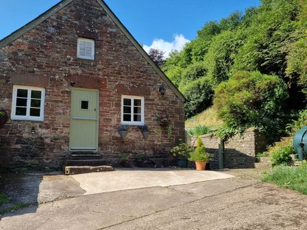 A cottage with a green door and flower planters at Anvil Cottage in Gatcombe near Blakeney