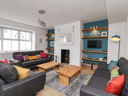 A living room with dark sofas and colorful cushions around wooden coffee tables at 2A Front Street Embleton