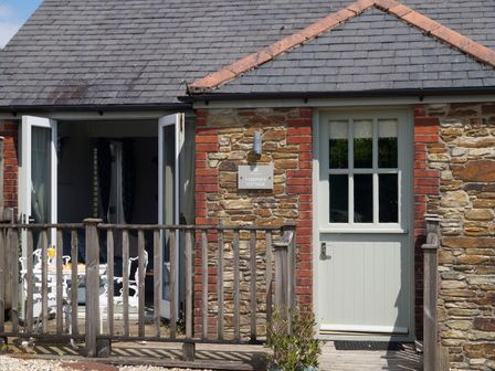A cottage entrance with a wooden door and open French doors showing a white outdoor table and chairs at 1 Keepers Cottage Hillfield Village Hillfield near Dartmouth