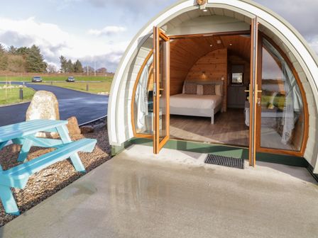An open pod with a bed inside and a blue picnic table outside at The Wheelhouse Pod No 4 Burtonport County Donegal