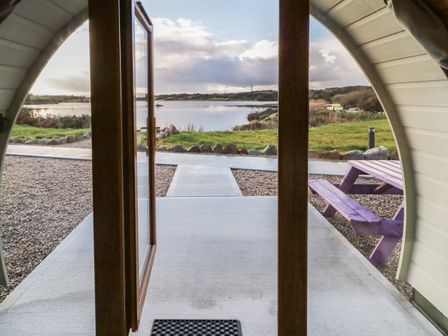 A view from inside a pod with a door opening to a path leading to a lake with a purple picnic table nearby at The Wheelhouse Pod No 5 Burtonport County Donegal