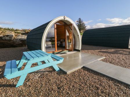 A curved pod cabin with glass door and blue picnic table outside at The Wheelhouse Pod No 6 Burtonport County Donegal