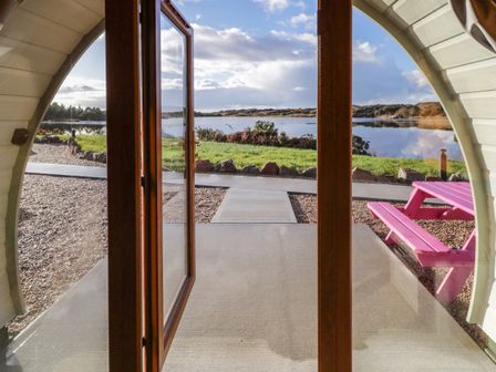 View through open wooden framed glass door of a patio with a pink picnic table and lake beyond at The Wheelhouse Pod No 8 Burtonport County Donegal