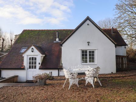 A white cottage with a tiled roof and outdoor white metal table and chairs on gravel at The Little White Cottage in Milton-Under-Wychwood