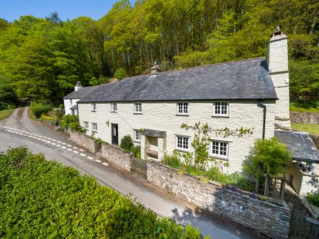 A long white stone house with slate roof along a narrow road surrounded by trees at Trentishoe Coombe in Parracombe