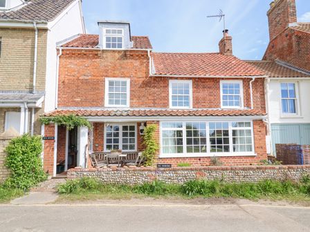 A red brick house with white window frames and a patio area at Beta Cottage in Walberswick