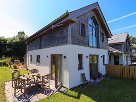 An outdoor patio area with a wooden dining table and chairs beside a two-story house with wood and plaster exterior at South Holm in Moreleigh