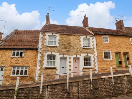 A row of stone cottages with tiled roofs and painted doors on a sloped street at Pendennis in Sherborne