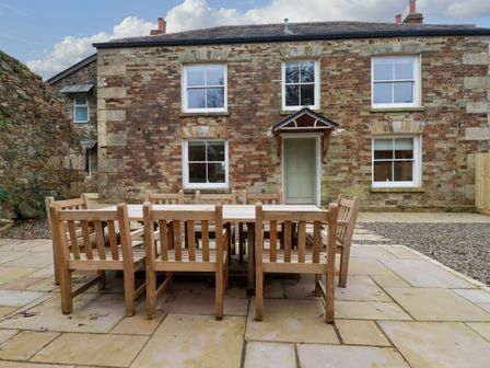 An outdoor patio with a wooden table and chairs in front of a stone house at Tretoil Farm House in Bodmin