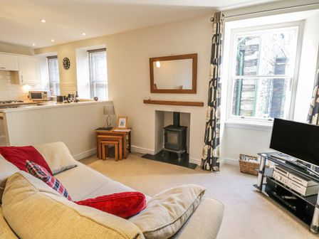 A living room with a beige sofa a wood burning stove and a television at La'l Tethera in Ambleside