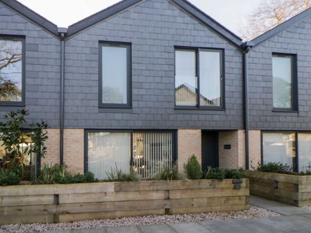 A modern two story house with black framed windows and wooden planters at Driftwood in Dawlish