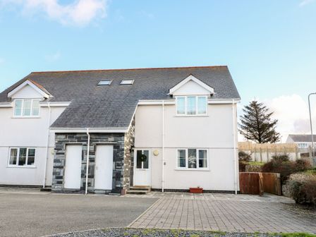 A two-story semi-detached house with a tiled roof two white doors a white main door and several windows at Ger Y Lli in Rhosneigr