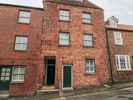 A red brick building with multiple white framed windows and green doors on a sloped street at Hidden Gem in Whitby