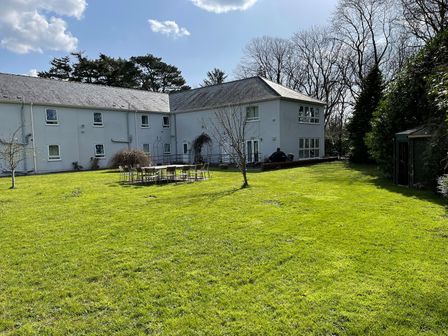 A large house with multiple windows and outdoor chairs arranged in a circle on a grassy lawn at Cadwaladr in Bontnewydd near Caernarfon