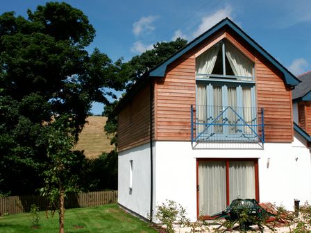 A two-story house with wooden paneling on the upper floor and white walls on the lower floor with a small balcony and garden furniture at Haven in Carnon Downs