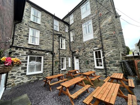An outdoor courtyard with wooden picnic tables and stone buildings at The Lombard in Dolgellau