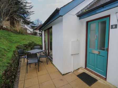 A patio area with a table and four chairs next to a building with a teal door at Villa Gallery in Carnon Downs
