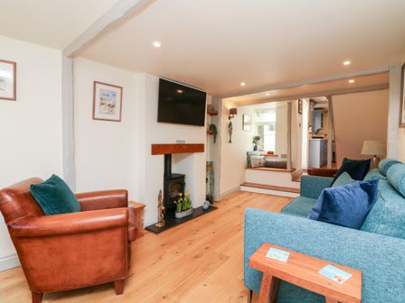 A living room with wooden floor a teal sofa a brown leather armchair a wood stove under a mounted tv and a built in seating area at Pepper's Cottage in Appledore