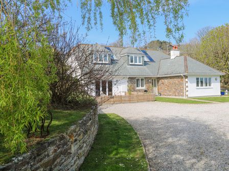 A stone house with a gravel driveway and green lawn surrounded by trees at Mariners Rest in Gorran Haven