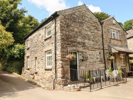 A stone house with white windows black door and exterior seating behind a metal fence at The Granary in St Breward near St Tudy