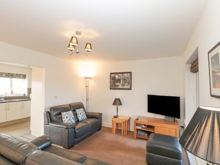 A living room with two leather sofas a wooden TV stand side tables lamps and a painting at Waddleduck in Whitby