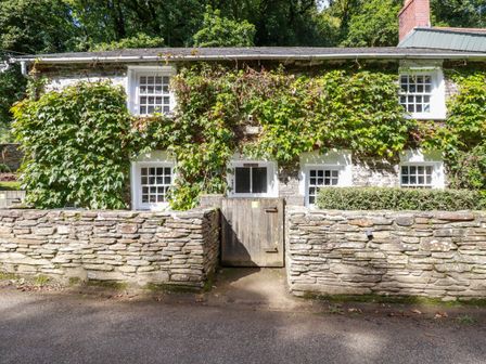 A stone cottage with ivy on the walls multiple white framed windows and a wooden gate at Willow View in Polmorla near Wadebridge