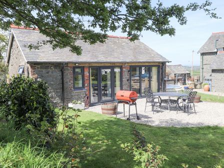 An outdoor patio area with a barbecue grill metal table and chairs in front of a stone house at Ael-y-bryn in Boduan near Tudweiliog