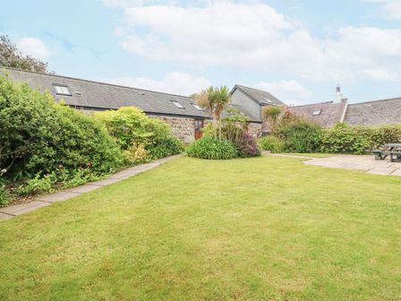 A garden with lawn shrubs and stone buildings in the background at The Old Dairy in Sarn Bach near Abersoch
