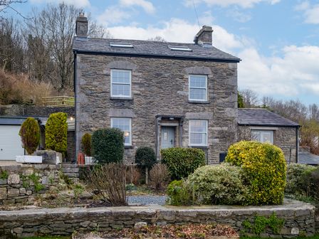 A stone house with four windows and a front door surrounded by trimmed bushes and trees at Sunny Brae in Lindale