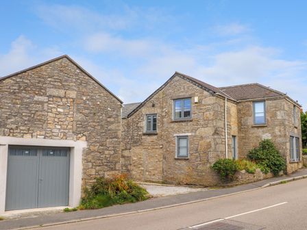 Stone houses with grey windows and a garage door by the roadside at Nancherrow Studio in St Just